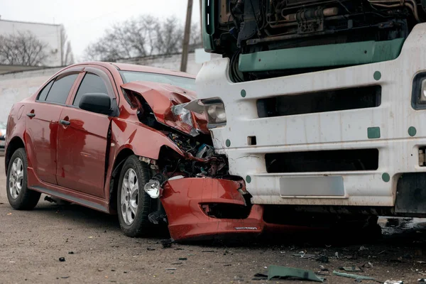 Bir araba ve kamyon arasındaki kafa kafaya çarpışmadan sonra. Kırmızı araba ağır hasar görmüş: kaput parçalanmış, far ve tampon kırılmış ve parçalar yola saçılmış..