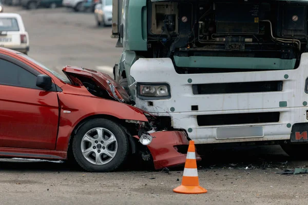 Bir araba ve kamyon arasındaki kafa kafaya çarpışmadan sonra. Kırmızı araba ağır hasar görmüş: kaput parçalanmış, far ve tampon kırılmış ve parçalar yola saçılmış..