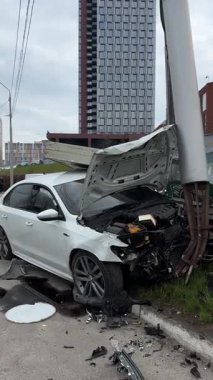 Ağır hasarlı bir araba, şehir yolunda kaza. Araba direğe çarpmış, ön taraf parçalanmış, kaput açık. Kaza kavramı, yoldaki tehlike ve sigorta..