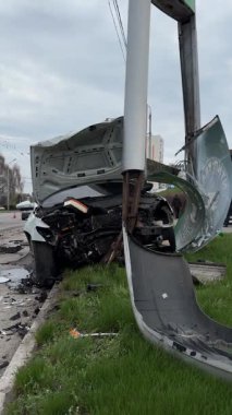Ağır hasarlı bir araba, şehir yolunda kaza. Araba direğe çarpmış, ön taraf parçalanmış, kaput açık. Kaza kavramı, yoldaki tehlike ve sigorta..