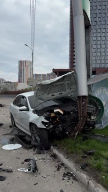 Ağır hasarlı bir araba, şehir yolunda kaza. Araba direğe çarpmış, ön taraf parçalanmış, kaput açık. Kaza kavramı, yoldaki tehlike ve sigorta..