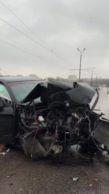 Islak bir yolda kaza yaptıktan sonra kaza yapmış siyah bir araba. Ön tarafı parçalanmış ve kaputu açık bir araba şehir caddesinde. Yağmurlu hava.