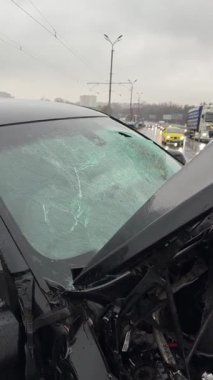 Islak bir yolda kaza yaptıktan sonra kaza yapmış siyah bir araba. Ön tarafı parçalanmış ve kaputu açık bir araba şehir caddesinde. Yağmurlu hava.