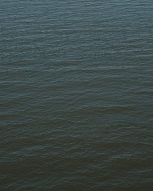 Sakin suyun yüzey dokusu, ince dalgalanmalar ve yumuşak yansımalarla, inceliklidir. Suyun koyu mavi ve gri renkleri huzur ve sükunet ortamı yaratır..