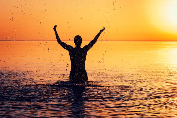 Man's silhouette in calm water at sunset. Man splashing water and enjoying nature