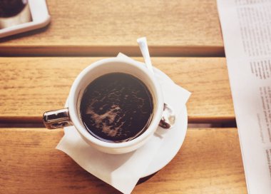 Bir fincan kahve ahşap masa üzerinde bir akıllı telefon ve gazete parçası ile