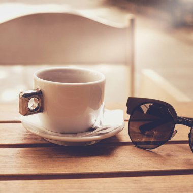 Bir fincan kahve ile bir parça ahşap bir masa üzerinde güneş gözlüğü ile açık kompozisyon