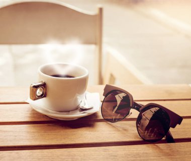 Açık kompozisyon ile bir fincan kahve ve ahşap bir masa üzerinde güneş gözlüğü