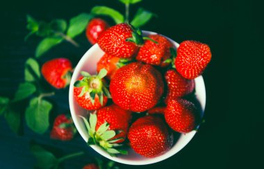 Taze kırmızı çilekli beyaz kase ve koyu bir ahşap üzerinde nane.