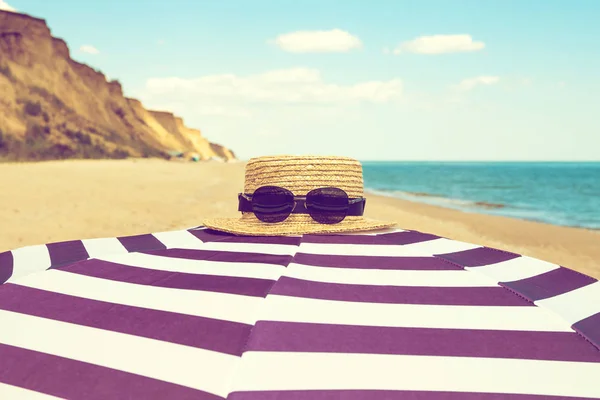 Ριγέ ομπρέλα παραλίας με ψάθινο καπέλο και γυαλιά ηλίου στη θάλασσα — Φωτογραφία Αρχείου