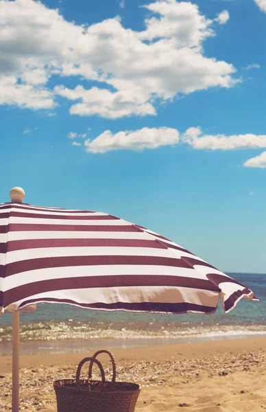 Gestreifter Sonnenschirm am Meeresufer mit Sand, Wasser und Wasser — Stockfoto