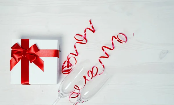 Two chrystal champagne glasses and a gift box tied with a red ri — Stock Photo, Image