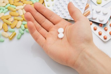 Adamın elinde bir sürü ilaç var, arka planda ilaç kutuları..