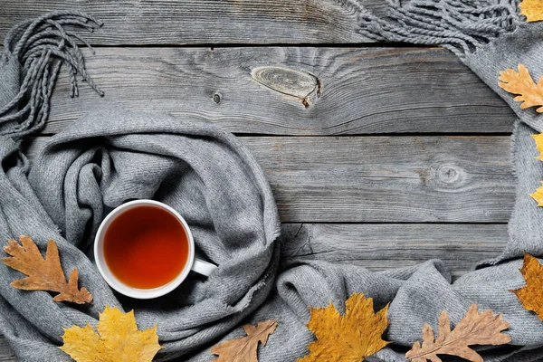 Autumn composition, fall leaves, hot steaming cup of tea and a warm scarf on wooden table background — Stock Photo, Image