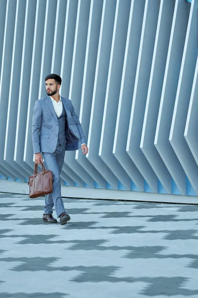 Businessman in formal wear with leather bag walking in city