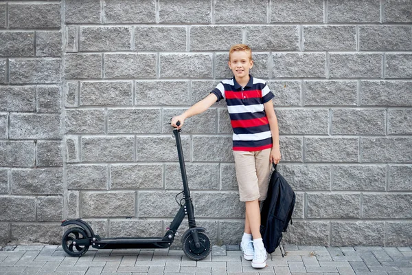 Sırt çantası ile şehirde onun elektrikli scooter ile ayakta okullu çocuk — Stok fotoğraf