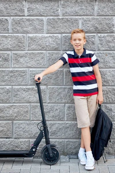 Jongen van de school in staat met zijn elektrische scooter in de stad met rugzak — Stockfoto