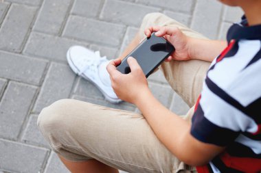Dış okul oturma ve cep telefonundan oyun çocuk