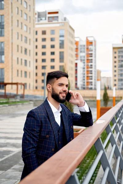 Bearded businessman speaks by phone and laughs.Young attractive business man using smartphone. Businessman talking on cell phone with customers