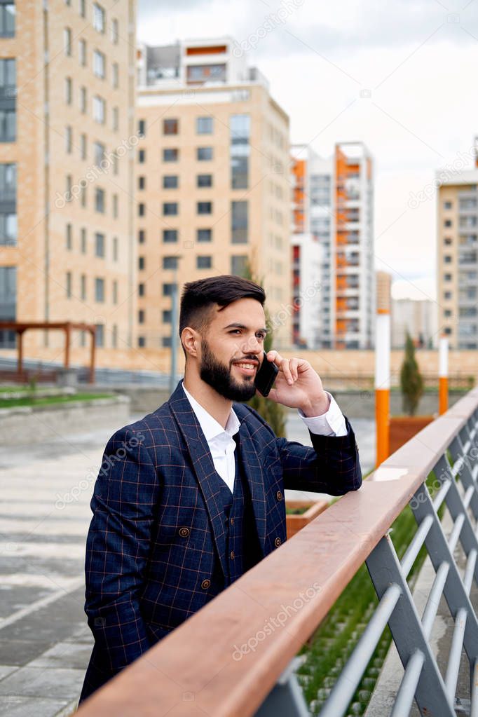 Bearded businessman speaks by phone and laughs.Young attractive business man using smartphone. Businessman talking on cell phone with customers