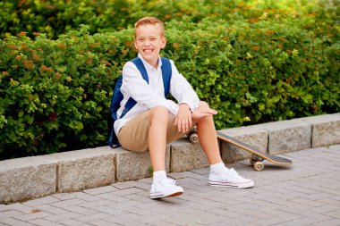 Sırt çantası ve açık havada kaykay ile mutlu gülümseyen okullu çocuk. Çocukluk, eğlence, okul ve insanlar kavramı