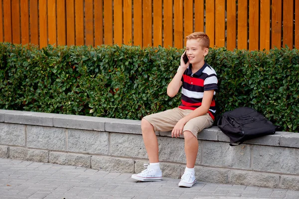 Dış okul oturma ve smartphone üzerinde konuşurken çocuk — Stok fotoğraf
