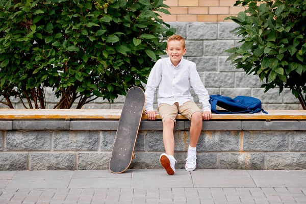 Feliz niño sonriente con mochila y monopatín al aire libre. Concepto de infancia, ocio, escuela y personas — Foto de Stock