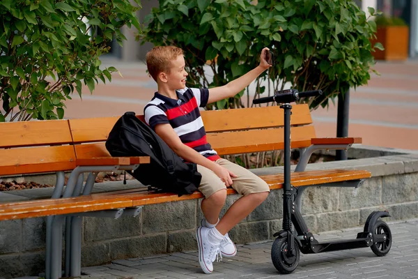 Menino da escola sorridente feliz com mochila e scooter elétrico ao ar livre. Conceito de infância, lazer, escola e pessoas — Fotografia de Stock