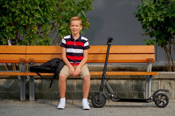Gelukkig lachend school jongen met rugzak en elektrische scooter buitenshuis. Jeugd, vrijetijdsbesteding, school en mensen concept — Stockfoto