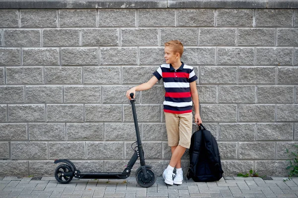 Jongen van de school in staat met zijn elektrische scooter in de stad met rugzak — Stockfoto