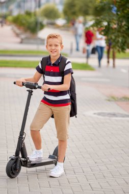 Güneşli sırt çantası ile şehirde onun elektrikli scooter ile Binicilik Okulu çocuk. Çocuk okula giderken bisikleti renkli giysiler içinde