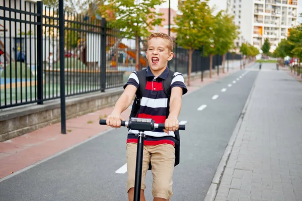 Güneşli sırt çantası ile şehirde onun elektrikli scooter ile Binicilik Okulu çocuk. Çocuk okula giderken bisikleti renkli giysiler içinde — Stok fotoğraf