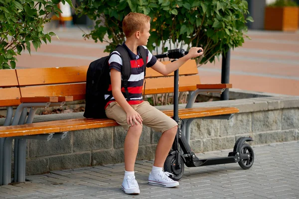 Gelukkig lachend school jongen met rugzak en elektrische scooter buitenshuis. Jeugd, vrijetijdsbesteding, school en mensen concept — Stockfoto