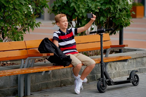 Gelukkig lachend school jongen met rugzak en elektrische scooter buitenshuis. Jeugd, vrijetijdsbesteding, school en mensen concept — Stockfoto