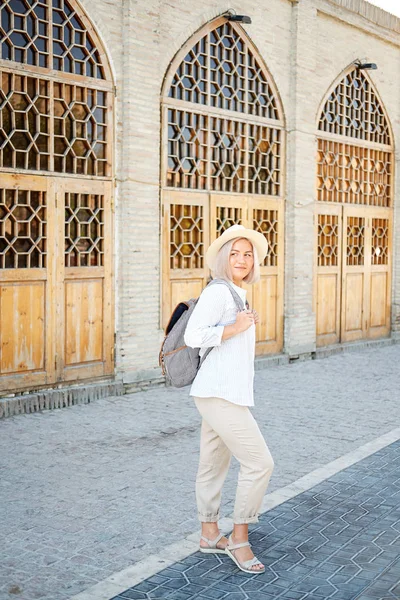 Jonge vrouwelijke reiziger met rugzak en hoed op de straat. Travel concept. Buchara, Oezbekistan — Stockfoto