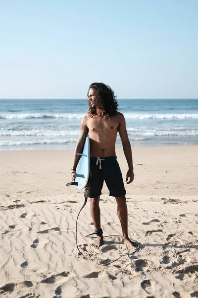 Surfista con tavola da surf sulla spiaggia. Razza mista pelle nera e barba. Attività sportive estive — Foto Stock