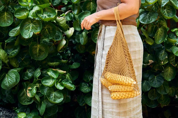 Kvinnan bär färska sockermajs i återanvändbara netto väska — Stockfoto