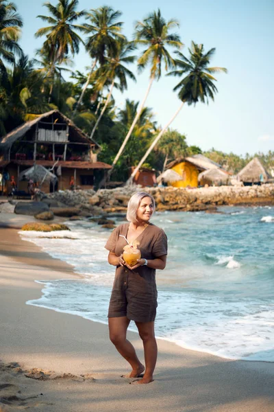 Woman Drink Coconut Juice at Tropical Beach. Happy Lady Enjoy Exotic Fresh Coco Cocktail on Seascape with Palm Rock. Female Tourist Smile. Summer Travel Paradise Landscape