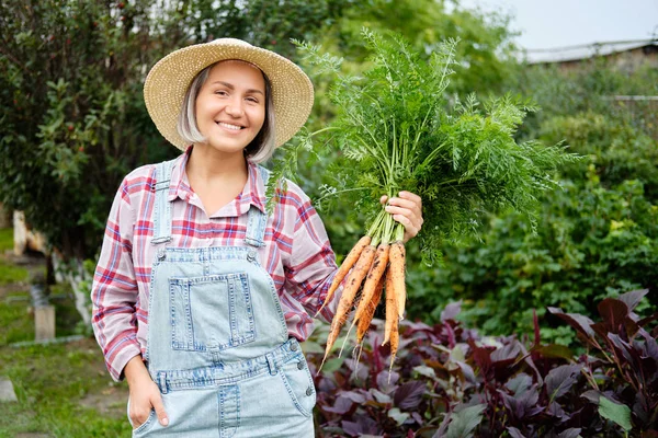 Cute girl in wearing Hat Picking Carrots in a Garden. Autumn Vegetable Harvest — Stock Photo, Image