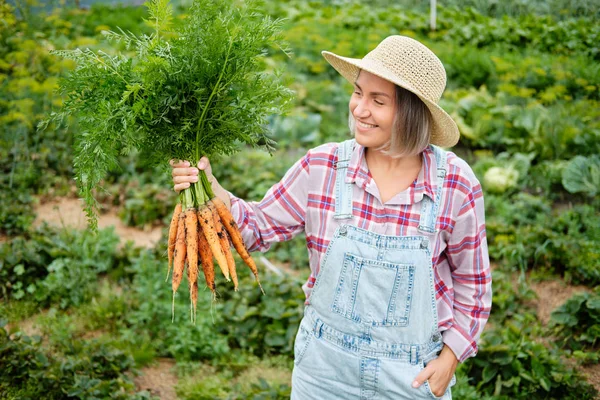 Jolie fille en portant chapeau cueillette de carottes dans un jardin. Récolte de légumes d'automne — Photo