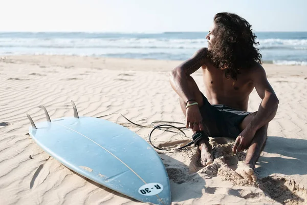 Surfista uomo seduto alla tavola da surf sulla spiaggia di sabbia — Foto Stock