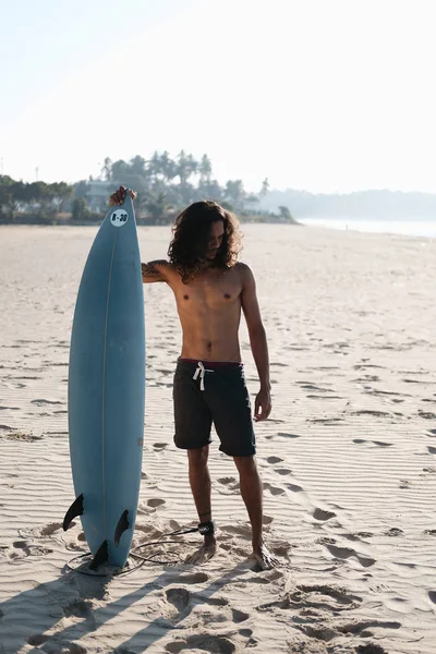 Hombre Surfista sentado en la tabla de surf en la playa de arena —  Fotos de Stock