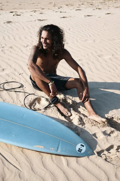 Surfista uomo seduto alla tavola da surf sulla spiaggia di sabbia — Foto Stock