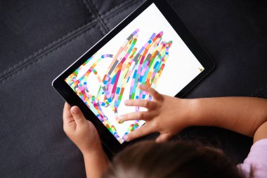 Anaokulu kızı tablete resim çizer. Küçük kız tabletle oynuyor.