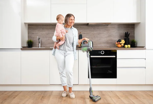 Aspirando y limpiando la casa. Madre feliz con su bebé en sus brazos. paternidad y maternidad. Cuidar a una mujer con un hijo. Trabajos domésticos —  Fotos de Stock