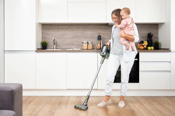 Vacuuming and Cleaning the House. Happy mother with her Baby in her Arms. Parenthood and motherhood. Caring woman with child. Housework — Stock Photo, Image