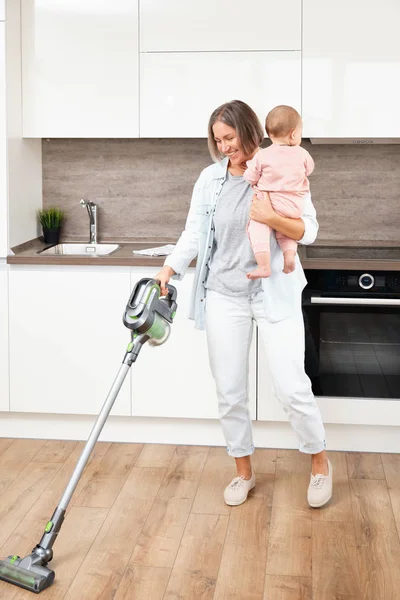 Aspirando y limpiando la casa. Madre feliz con su bebé en sus brazos. paternidad y maternidad. Cuidar a una mujer con un hijo. Trabajos domésticos —  Fotos de Stock