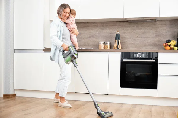 Aspirando y limpiando la casa. Madre feliz con su bebé en sus brazos. paternidad y maternidad. Cuidar a una mujer con un hijo. Trabajos domésticos —  Fotos de Stock