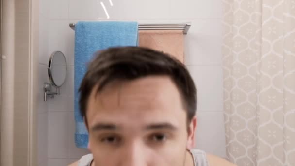Ospalý a chundelatý mladý muž s kocovinou se ráno podívá do zrcadla v koupelně — Stock video