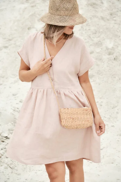 Stilvolles Mädchen im trendigen Sommerkleid aus Leinen mit Strohhut und Tasche posiert im Sand. Sommeroutfit — Stockfoto